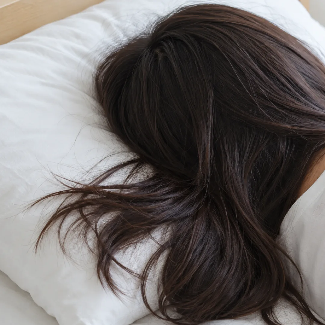 白い枕に横向きに頭をのせた人の後頭部と、枕の上に広がる長い茶色の髪。
