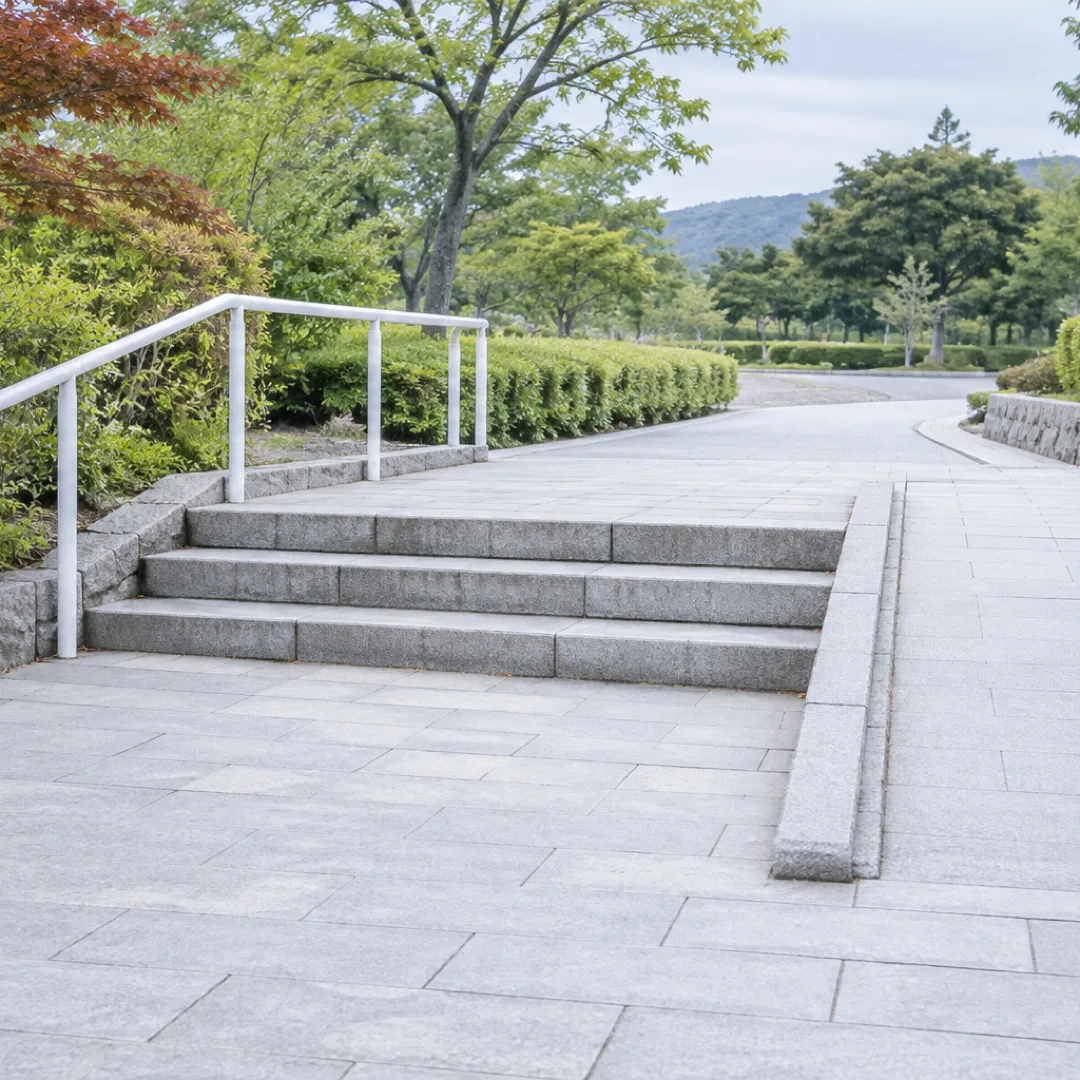 日本の静かな公園で、白い手すりのある低い石段と緩やかな坂道が並んでいる。