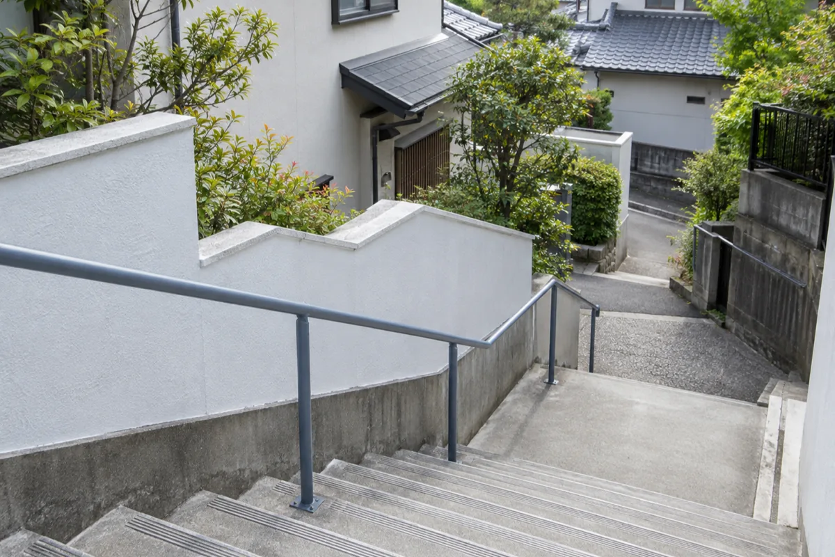 日本の住宅街にある、青灰色の手すりと白い壁に沿って下りる屋外階段。