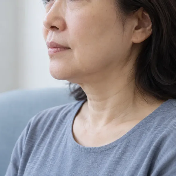 Close side view of a woman's lower cheek, jawline and neck against a pale blue and white background.