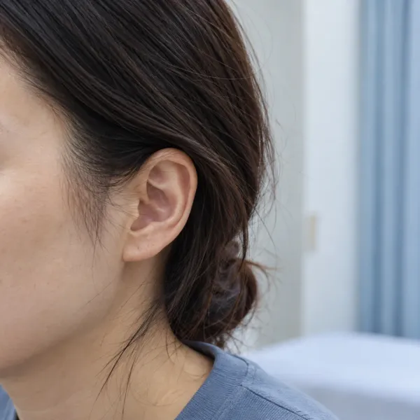 Side view of an adult’s temple and upper cheek, with hair tucked behind the ear in a softly lit consultation room.
